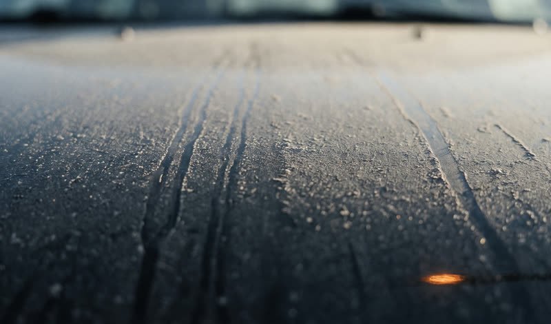 A neglected black car panel under a thick layer of road dust with old rain streaks running through it.